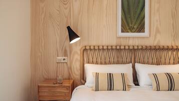 A neatly arranged bedroom with a wooden headboard, a bedside table with a lamp, and a framed plant on the wall.