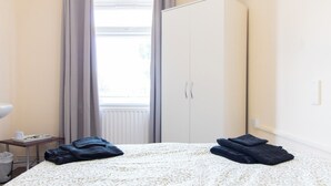 Quarto de hotel com cama, guarda-roupa, janela com cortinas e uma pequena mesa com bandeja.