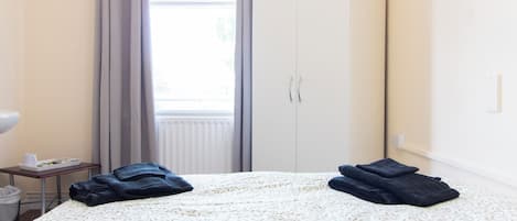 A hotel room with a bed, a wardrobe, a window with curtains, and a small table with a tray.