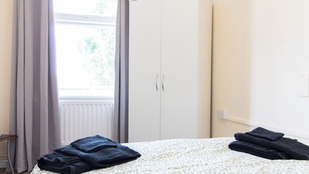 Quarto com cama, guarda-roupa e janela com cortinas.