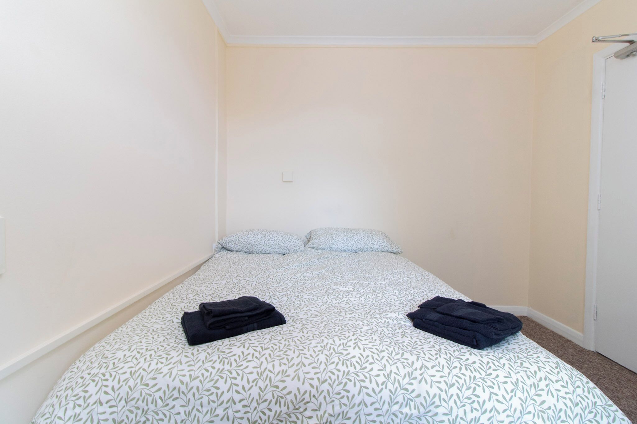 Une petite chambre avec un lit simple, une couvre-lit à motifs, deux oreillers et deux serviettes pliées posées sur le lit.