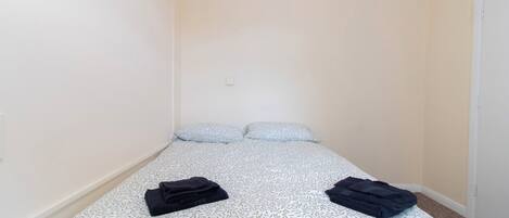 Una habitación pequeña con cama individual, una colcha estampada, dos almohadas y dos toallas dobladas sobre la cama.