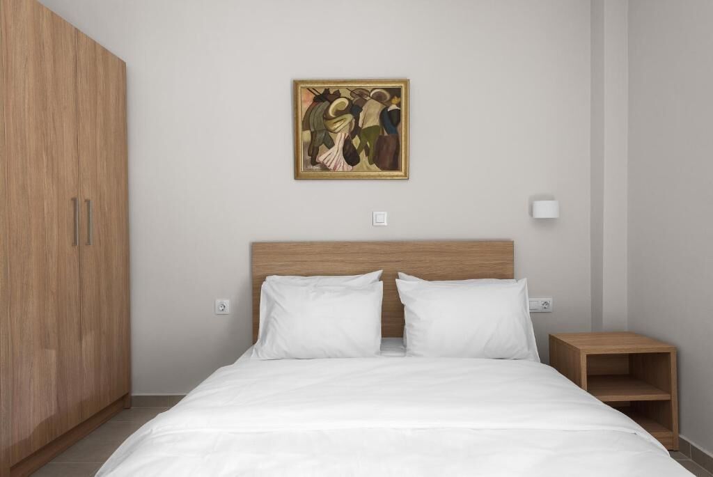 Un dormitorio con cama, armario de madera, mesita de noche y un cuadro en la pared.