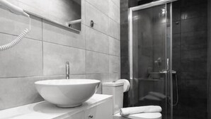 Un baño moderno con un lavamanos grande de color blanco, un inodoro y una ducha con mampara de vidrio.