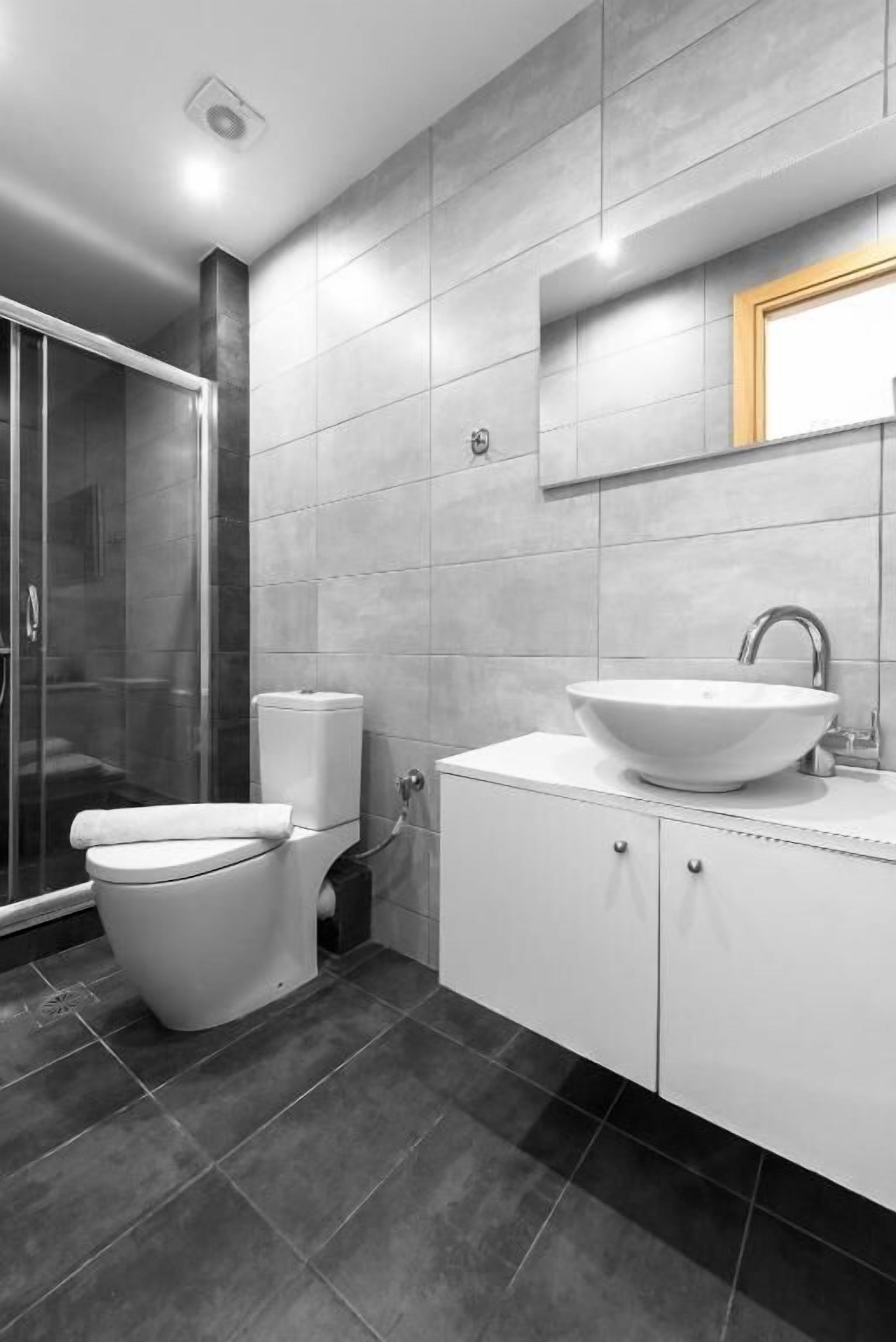 Un baño moderno con cabina de ducha de vidrio, inodoro blanco y lavabo con espejo.