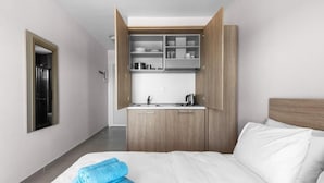 Habitación de hotel con cama, ropa de cama azul ordenada, armario de madera y zona de kitchenette.