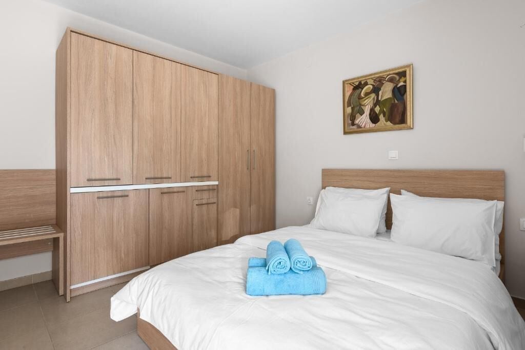 Un dormitorio con cama, ropa de cama blanca, un armario de madera y un cuadro en la pared.