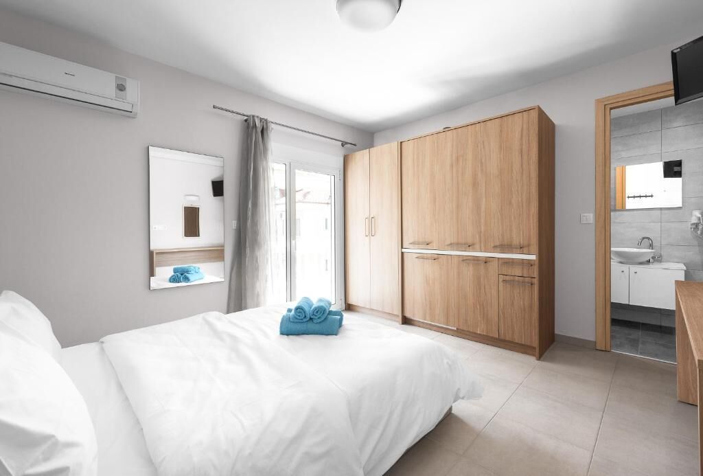 A hotel room with a bed, a wardrobe, a bathroom with a sink and mirror, and a television on the wall.