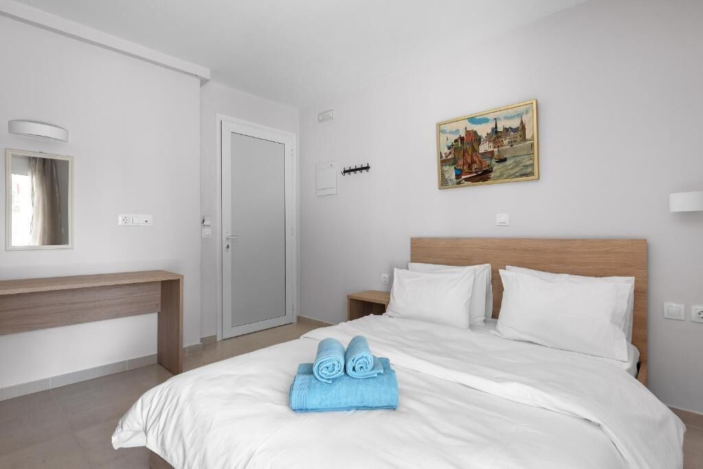 Una habitación de hotel con cama, mesita de noche, un cuadro en la pared y una puerta.