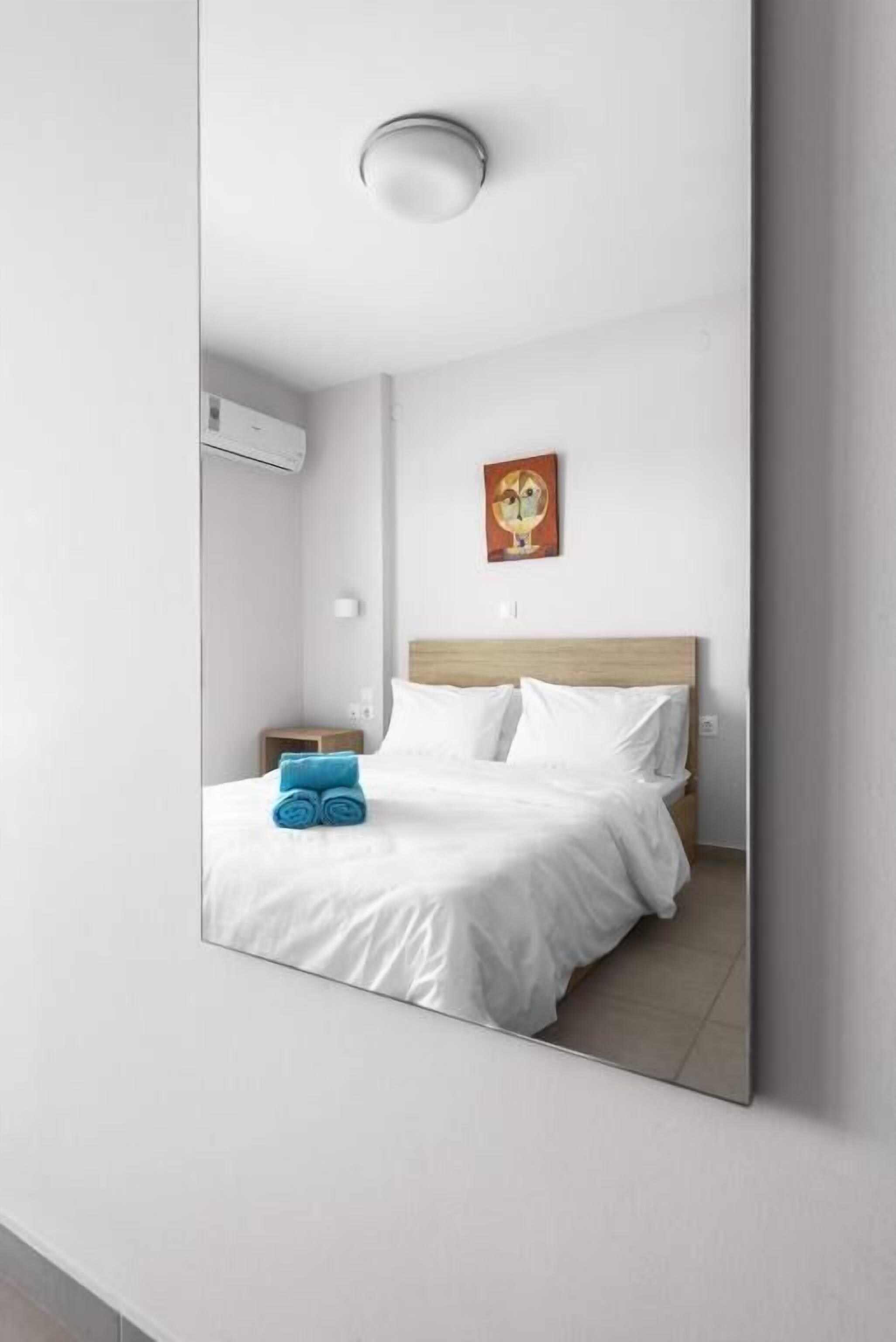 A modern hotel room with a large bed, a nightstand, a wall-mounted air conditioner, and a painting above the bed.