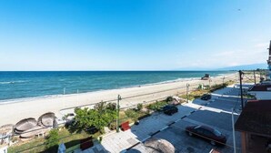 Vista costera con playa, un coche aparcado y un edificio con balcón que da al mar.