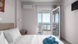 Habitación de hotel con cama, mesita de noche, televisor y balcón con vista al mar.
