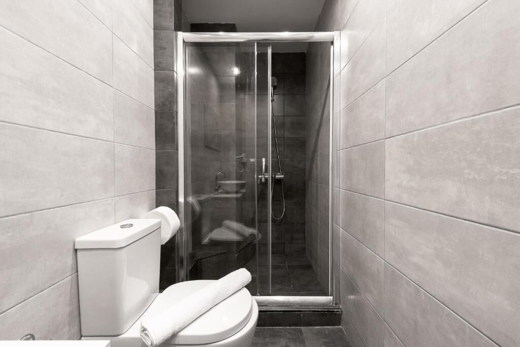 A modern bathroom with a toilet, a glass-enclosed shower stall, and tiled walls.