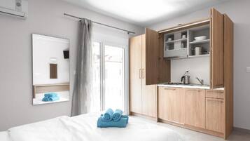 A modern hotel room with a bed, a bathroom mirror, a wardrobe, and a kitchenette.
