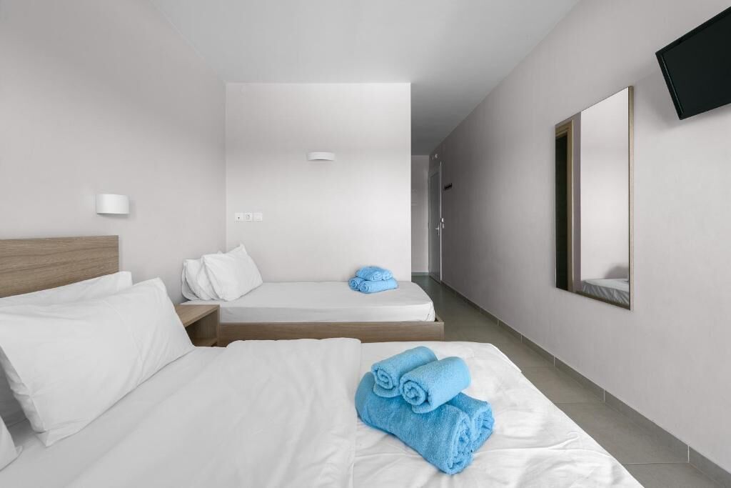 A hotel room with a large bed, a smaller bed, a wooden headboard, a flat-screen TV mounted on the wall, and a mirror.