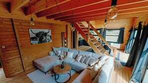 A cozy wooden interior with a sectional sofa, a round coffee table, and a staircase leading to an upper level. - Chalet "Les Alpages (Durbuy)