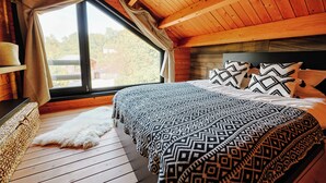 A cozy bedroom with a large window, wooden ceiling, and a bed with patterned bedding. - Chalet "Les Alpages (Durbuy)