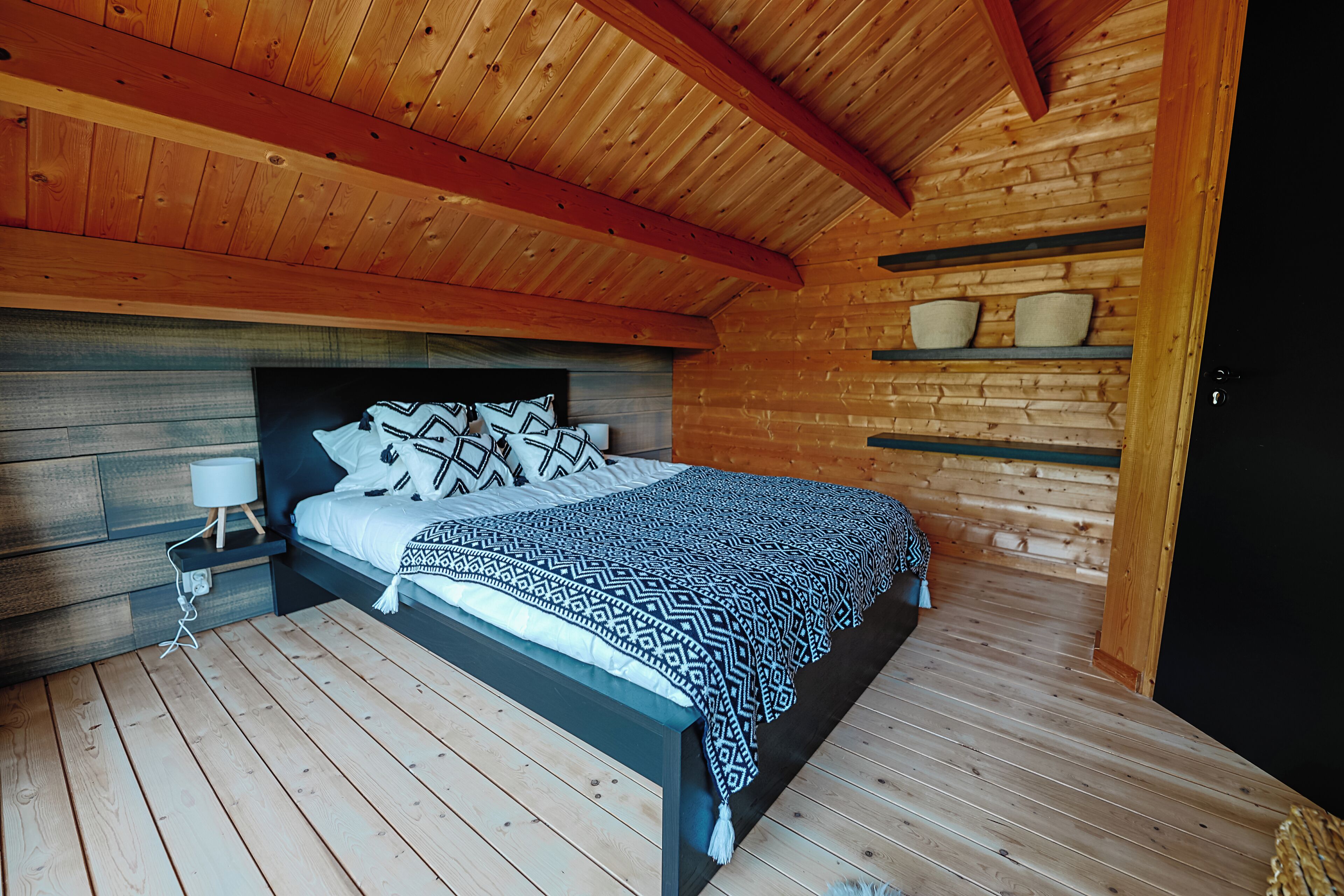 A wooden cabin bedroom with a bed, nightstand, and shelves with bowls.