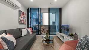 Ein modernes Wohnzimmer mit grauem Sofa, einem roten Sessel, einem Glastisch und einem Flachbildfernseher.