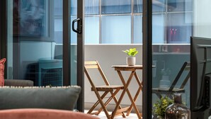 Ein Zimmer mit einer Schiebetür zum Balkon, einem kleinen Holztisch mit einer Pflanze und einem Stuhl.
