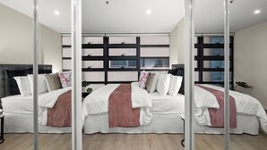 Ein modernes Schlafzimmer mit einem großen Bett, einer Glastrennwand und Blick auf die Stadt durch große Fenster.