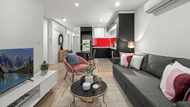 Ein modernes Wohnzimmer mit Flachbildfernseher, einer Couch, einem Couchtisch und einem Essbereich im Hintergrund.