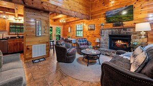 A log cabin interior with a fireplace, wooden walls, a dining area, and a living room with seating. - Dog OK | Hot Tub + Game Rm | Dollywood (Pigeon Forge)