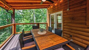 A wooden deck with a table and chairs, a ceiling fan, and a view of the forest. - Dog OK | Hot Tub + Game Rm | Dollywood (Pigeon Forge)