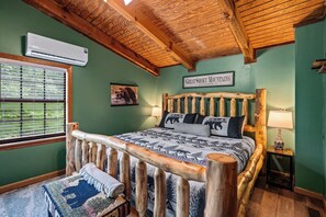 Une chambre à coucher rustique avec un cadre de lit en bois, un climatiseur fixé au mur, un tableau représentant un ours, et une fenêtre avec des stores.