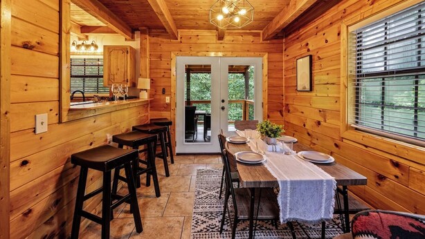 A wooden cabin interior with a dining area, bar, and large windows. - Dog OK | Hot Tub + Game Rm | Dollywood (Pigeon Forge)