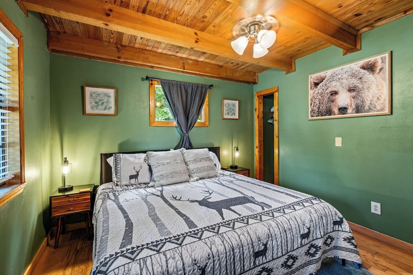 A bedroom with a large bed, wooden ceiling beams, a ceiling fan, and a bear picture on the wall.
