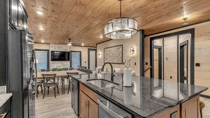 Una cocina moderna con una isla central, techo de madera y un comedor con sillas y una mesa.