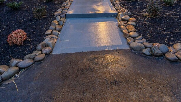 Una casa moderna de dos pisos con fachada de piedra, un balcón con luces colgantes y mobiliario exterior.