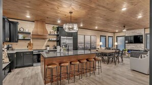 A modern kitchen with a large island, bar stools, and a dining area with a fireplace. - 10BR Luxury | 2 Cabins | Rooftop Lounges | Indoor Pools | Hot Tubs | Walk to Water Park | Sleeps 44 (Sevierville)