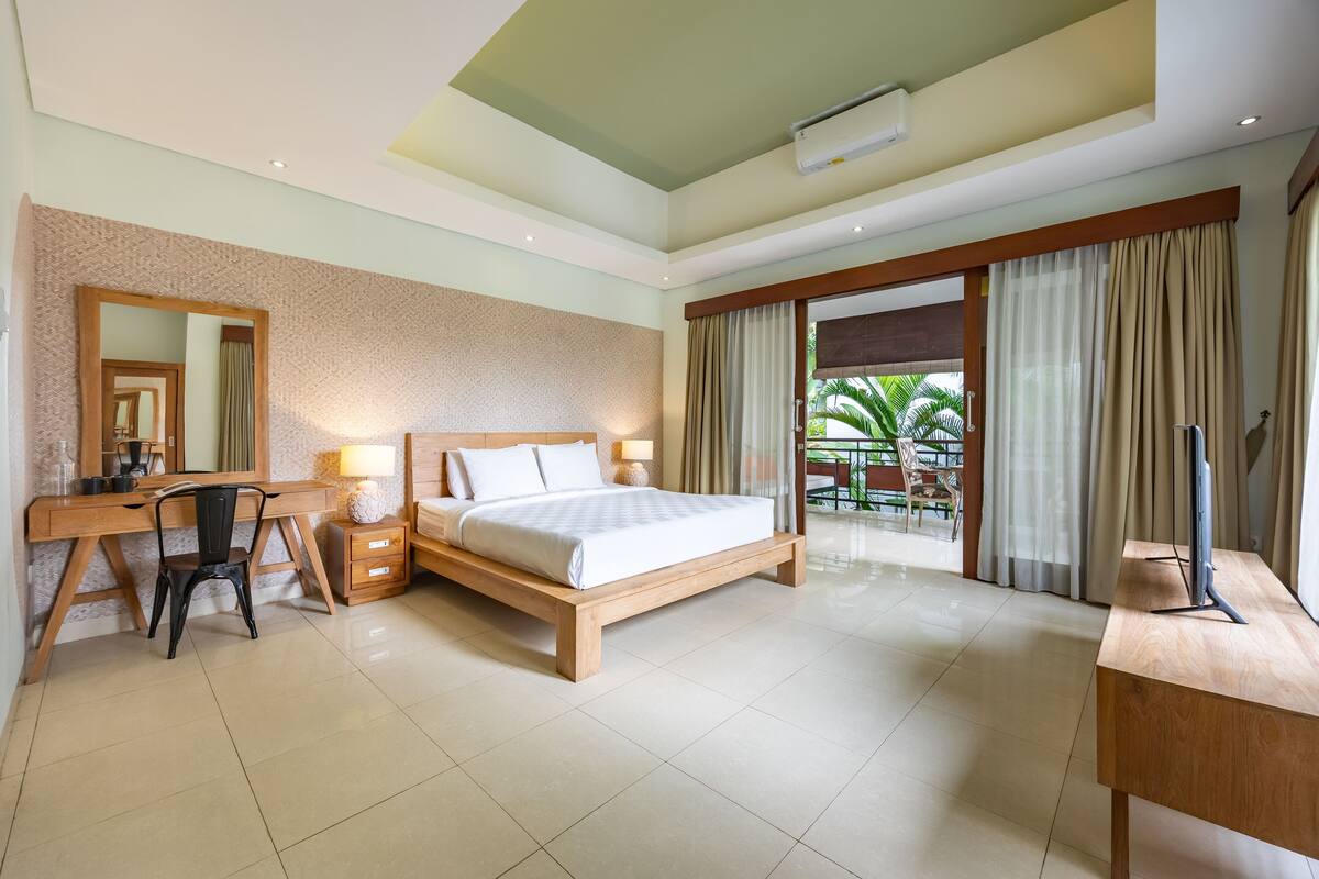 A hotel room with a wooden bed, a desk with a chair, a large mirror, and a TV.