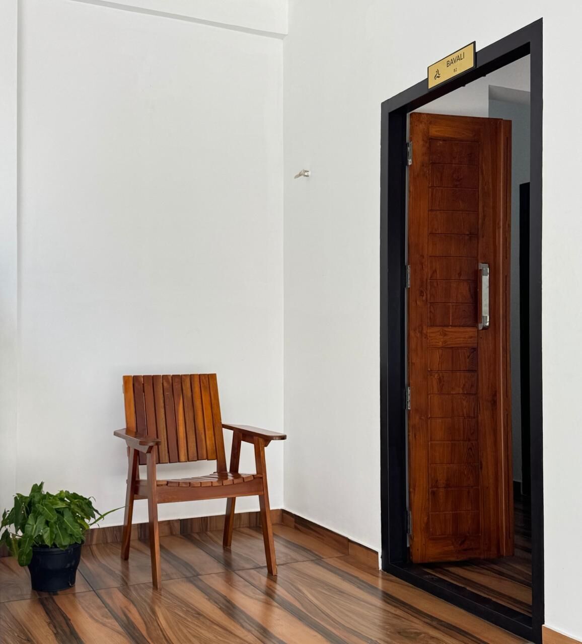A wooden chair and a potted plant in a room with a wooden floor and a wooden door with a sign above it.
