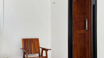 A wooden chair and a potted plant in a room with a wooden floor and a wooden door with a sign above it.