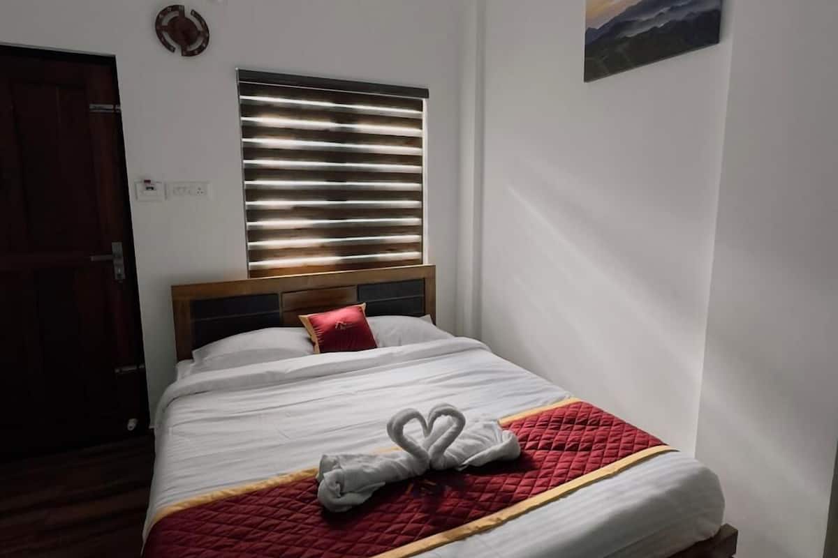 Una cama bien hecha con un edredón rojo, un cabecero de madera y una ventana con persianas.