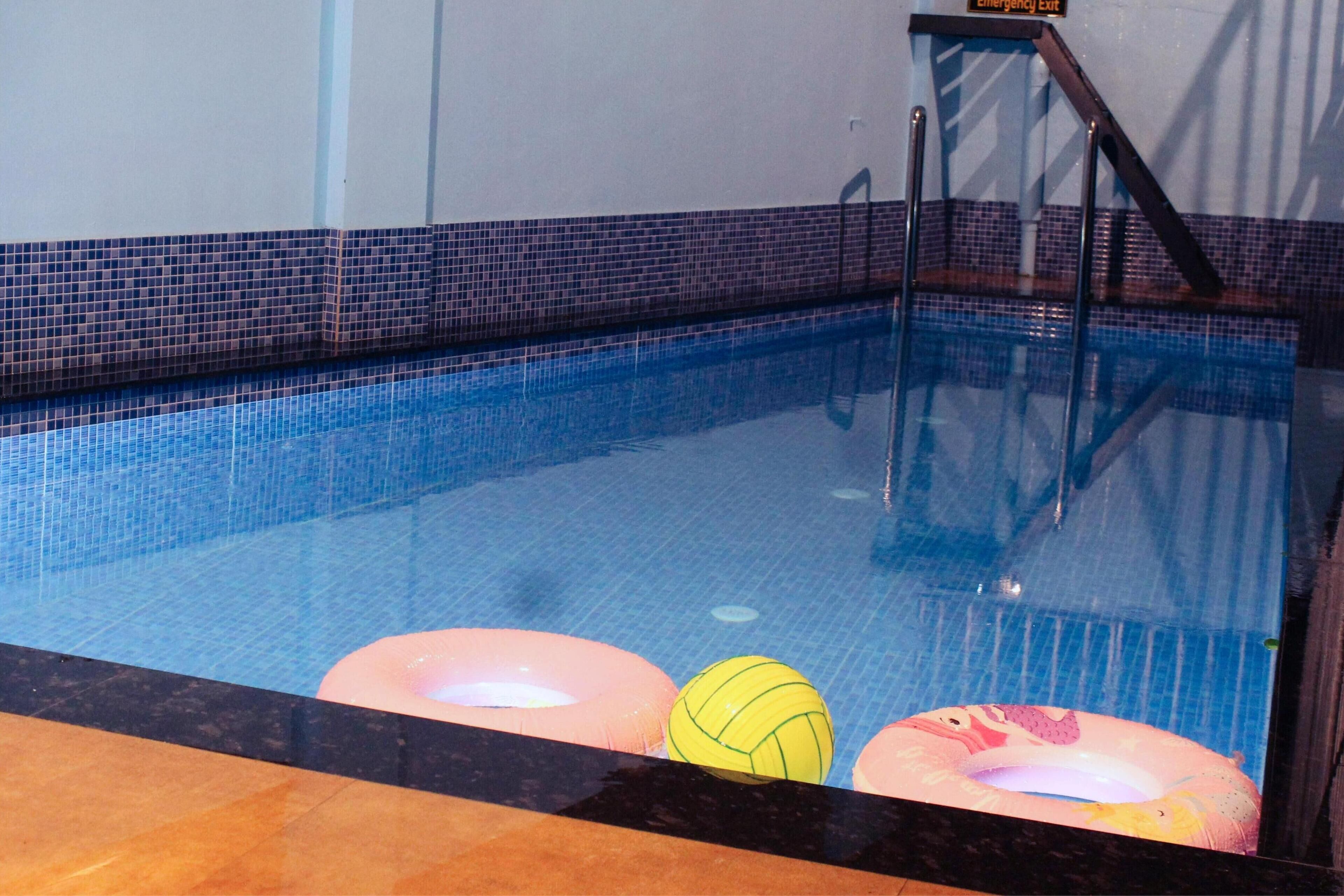 An indoor swimming pool with clear blue water, a tiled edge, and a safety exit sign.