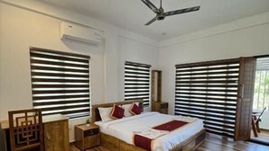 Une chambre à coucher avec un lit, un plancher en bois, un ventilateur de plafond et de grandes fenêtres équipées de stores.
