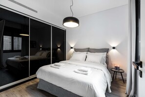 A modern bedroom with a large mirror, a bed with white linens, a round pendant light, and a small bedside table with candles. - Cozy 2BR Apartment  Near Syntagma Square (Athina)