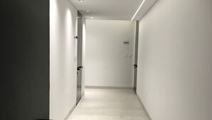 Een gang met witte wanden en een lichtgekleurde vloer, die leidt naar een deur met het nummer 492.