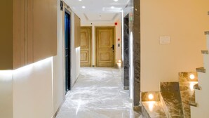 A hallway with marble flooring, wooden doors, and a staircase with illuminated handrails.