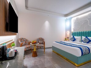 A modern hotel room with a bed, two chairs, a small table with fruit, and a TV.