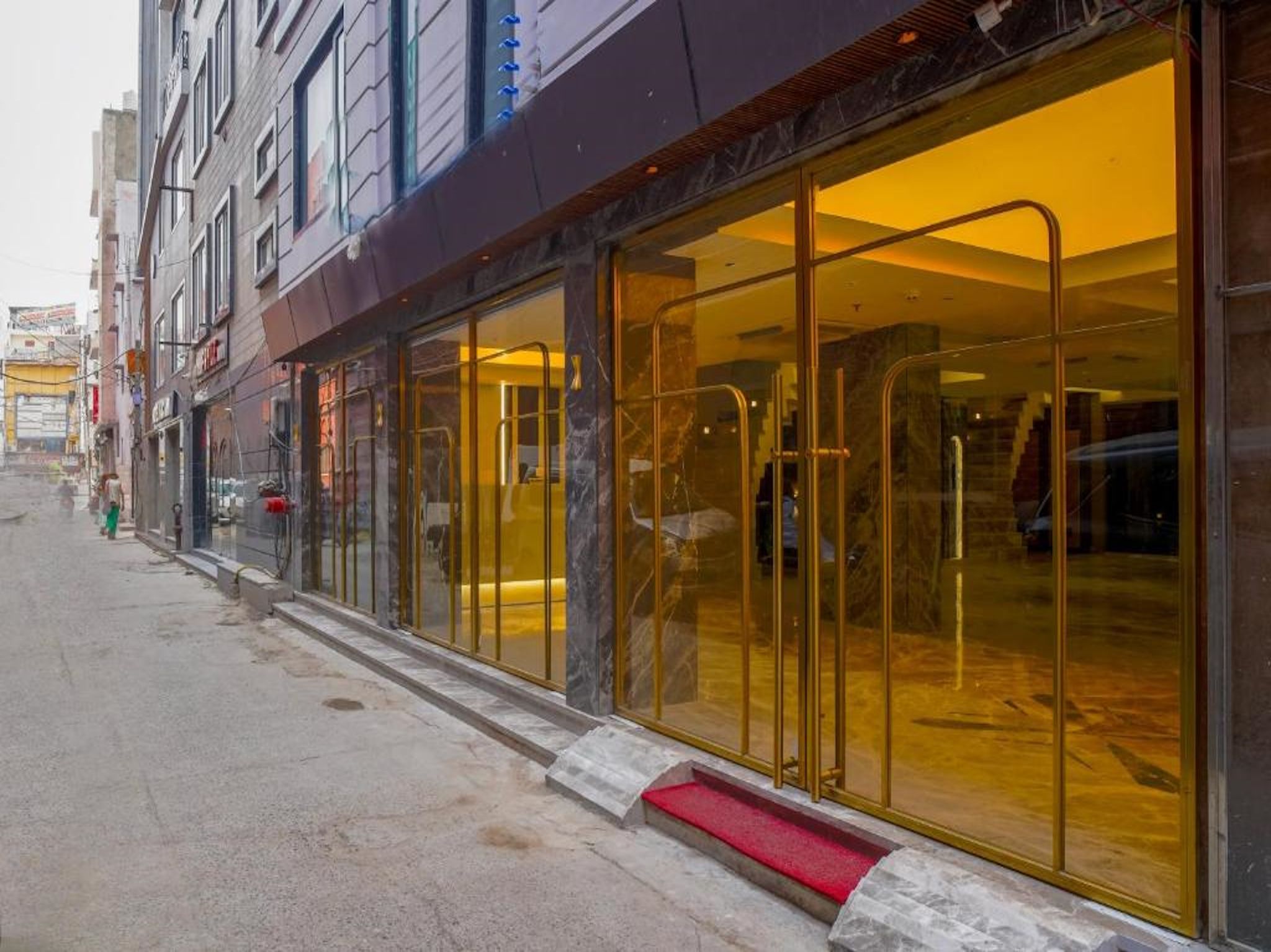 L’entrée d’un hôtel avec une façade en verre, un tapis rouge et un sol en marbre.