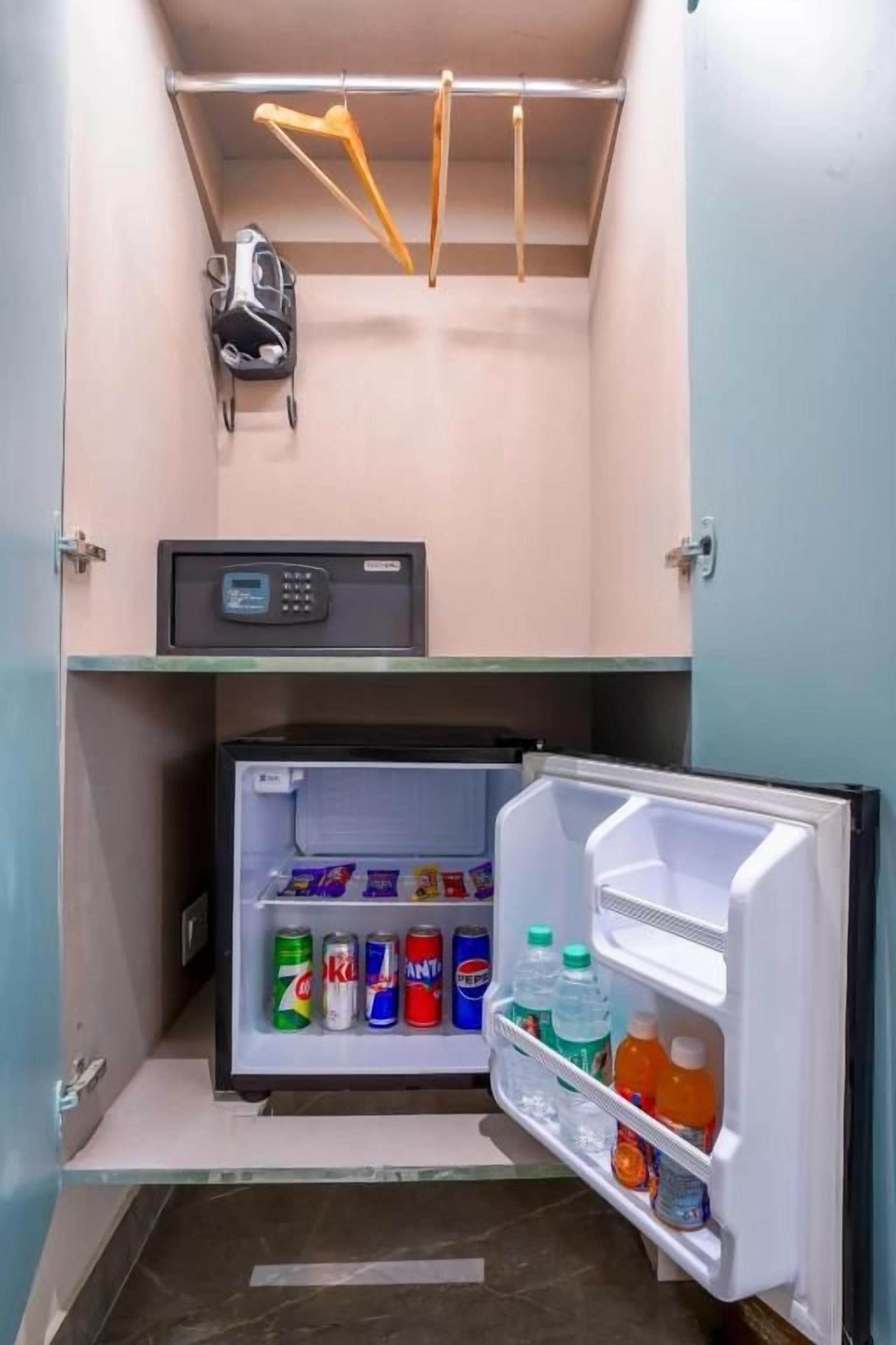 A compact refrigerator with a digital control panel, a microwave above it, and a small shelf with a helmet.
