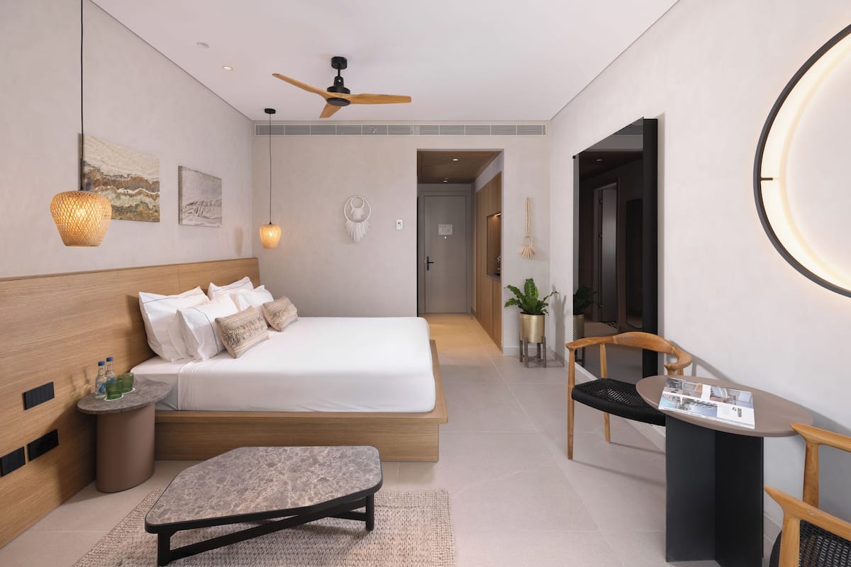 Un dormitorio moderno con cama, mesita de noche y una zona de lectura con sillón y mesa.