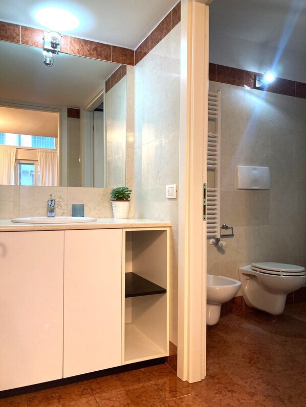 A bathroom with a sink, mirror, toilet, bidet, and a towel rack.