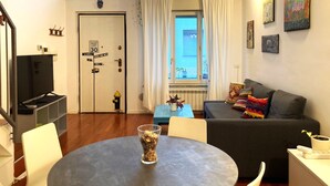 Una sala de estar moderna con un sofá gris, una mesa redonda con un vaso de cereal, un televisor y una puerta con un letrero de límite de velocidad en el pueblo.