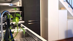 Una cocina moderna con un lavamanos de acero inoxidable, un refrigerador negro y una escalera que sube a un nivel superior.